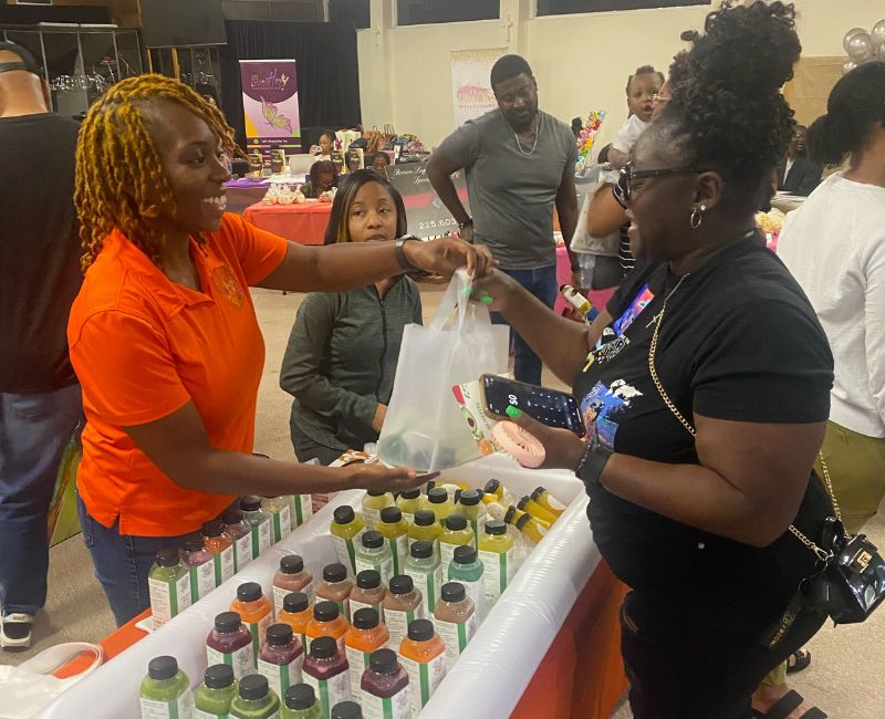 Shardai handing a shopping bag of cold pressed juice to a customer